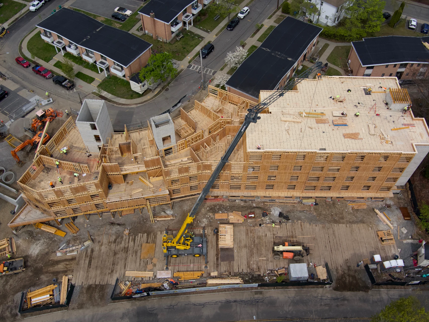 Overhead aerial view of a multi-story timber-framed building under construction, with a crane on site and surrounding streets and houses